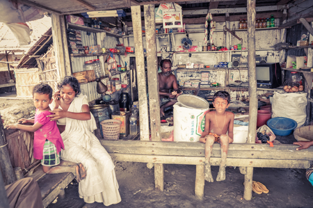Sunderban, Bangladesh - circa July 2012: Native family sits in their house and barefoot children look to photocamera in Sunderban, Bangladesh. Documentary editorial.のeditorial素材