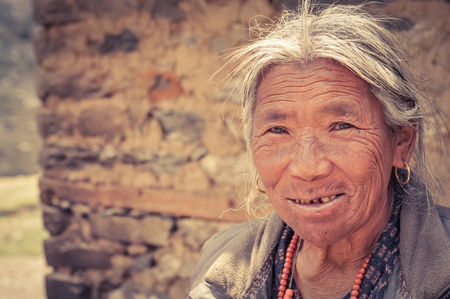Dolpo, Nepal - circa June 2012: Old grey-haired woman with wrinkles on face dressed in grey shirt wears golden earrings in Dolpo, Nepal. Documentary editorial.のeditorial素材