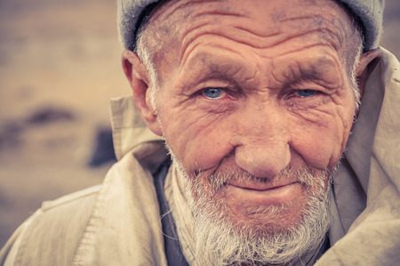 Karakul, Tajikistan - circa September 2011: Older native man with wrinkled face, beard and beautiful blue eyes filled with tears in Karakul, Tajikistan. Documentary editorial.のeditorial素材