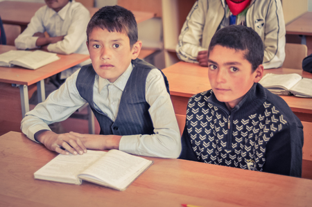 Khorog, Tajikistan - circa September 2011: Two young boys sit at desk and look to photocamera at school in Khorog, Tajikistan. Documentary editorial.のeditorial素材