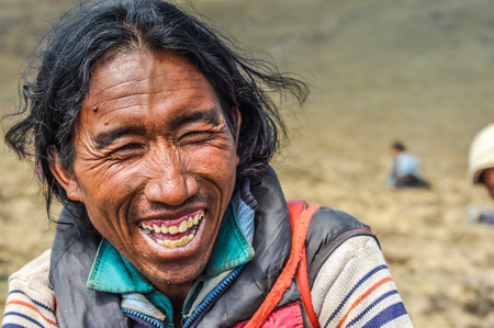 Dolpo, Nepal - circa June 2012: Native black-haired man dressed in jacket sits on ground and laughs joyfully in Dolpo, Nepal. Documentary editorial.のeditorial素材