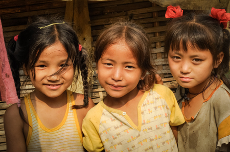 Damak, Nepal - circa May 2012: Photo of three young girls in yellow t-shirts standing next to each other and at Nepali refugee camp in Damak, Nepal. Documentary editorial.のeditorial素材