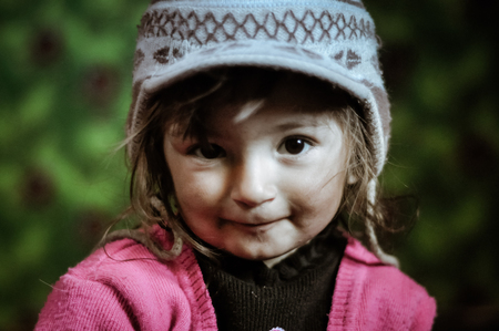 Khorog, Tajikistan - circa September 2011: Small girl with knitted cap and pink sweater looks with humble eyes to photocamera in Khorog, Tajikistan. Documentary editorial.のeditorial素材