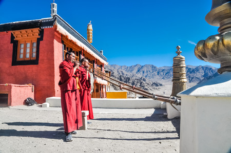 Thiksey, Ladakh - circa November 2011: Photo of two monks dressed in red blowing horns on roof as morning ceremony at Thiksey monastery, Ladakh. Documentary editorial.のeditorial素材