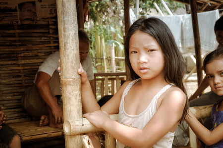 Damak, Nepal - circa May 2012: Young native girl with long black hair frowns to photocamera at Nepali refugee camp in Damak, Nepal. Documentary editorial.のeditorial素材