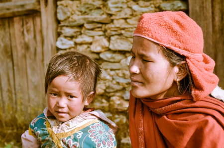 Beni, Nepal - circa May 2012: Photo of mother in red scarf and headcloth kneeling next to her small daughter with brown hair and brown eyes in Beni, Nepal. Documentary editorial.のeditorial素材