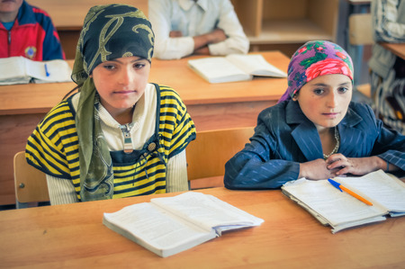 Khorog, Tajikistan - circa September 2011: Two young girls sit at desk at school in Khorog, Tajikistan. There are opened textbooks on desk. Documentary editorial.のeditorial素材
