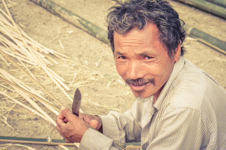 Damak, Nepal - circa May 2012: Old man dressed in white clothes holds knife at Nepali refugee camp in Damak, Nepal. Documentary editorial.のeditorial素材