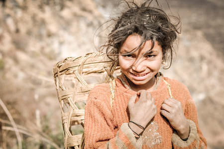 Kuari pass, Uttarakhand - circa December 2011: Young native girl dressed in orange sweater carries basket on her back in Kuari pass, Uttarkhand. Documentary editorial.のeditorial素材