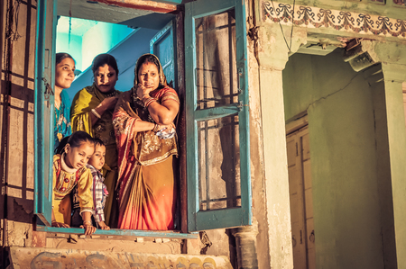 Bikaner, Rajasthan - circa December 2011: Women and children stand and look curiously out of window to wedding ceremony in Bikaner, Rajasthan. Documentary editorial.のeditorial素材