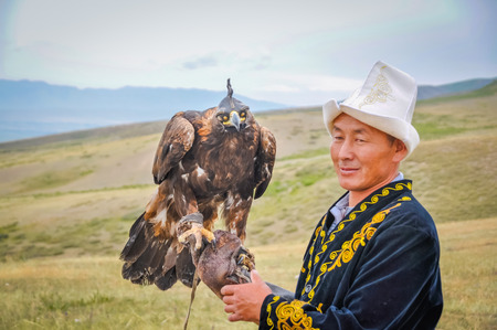 Karakol, Kyrgyzstan - circa July 2011: Native man dressed in traditional folk costume poses with Golden eagle on his arm at Karakol festival in Kyrgyzstan. Documentary editorial.のeditorial素材