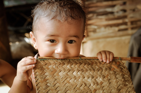 Damak, Nepal - circa May 2012: Photo of small cute boy looking to photocamera and holding wooden stick in his mouth at Nepali refugee camp in Damak, Nepal. Documentary editorial.のeditorial素材