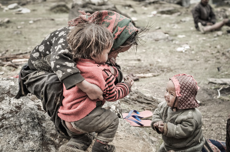 Dolpo, Nepal - circa June 2012: Small children in warm sweaters kneel and play together on ground outside in Dolpo, Nepal. Documentary editorial.のeditorial素材