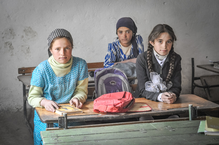 Khorog, Tajikistan - circa September 2011: Three young girls sit at desk at school and look to photocamera in Khorog, Tajikistan. Documentary editorial.のeditorial素材
