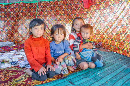 Arslanbob, Kyrgyzstan - circa July 2011: Small native siblings in colourful clothes sit on the ground in Arslanbob, Kyrgyzstan. Documentary editorial.のeditorial素材