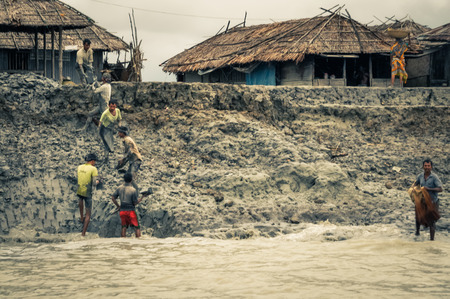 Sunderban, Bangladesh - circa July 2012: Native men work in mud near their houses and river in Sunderban, Bangladesh. Documentary editorial.のeditorial素材