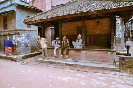 Bhaktapur, Nepal - circa June 2012: Four native men wth traditional caps on heads sit and talk outside in Bhaktapur, Nepal. Documentary editorial.のeditorial素材