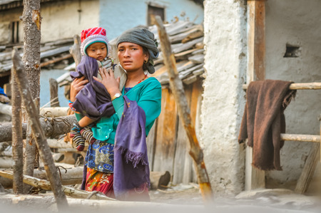 Dolpo, Nepal - circa May 2012: Native woman with grey headcloth wears green sweatshirt and holds her child covered in violet scarf and with red cap and she in Dolpo, Nepal. Documentary editorial.のeditorial素材