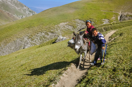 Arslanbob, Kyrgyzstan - circa July 2011: Smiling native children pose with donkey at top of hill in mountain range of Arslanbob, Kyrgyzstan. Documentary editorial.のeditorial素材