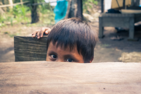 Mashaquipe, Bolivia - circa June 2009: Young native boy looks timidly and hides behind table at Mashaquipe, Bolivia. Documentary editorial.のeditorial素材