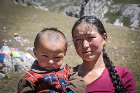 Arslanbob, Kyrgyzstan - circa July 2011: Young woman with long braid of hair poses with her child in Arslanbob, Kyrgyzstan. Documentary editorial.のeditorial素材