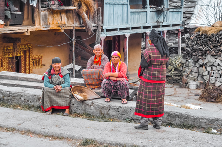 Manali, Himachal Pradesh - circa November 2011: Three native women with headcloths sit on ground and one woman stands near them in Manali. Documentary editorial.のeditorial素材