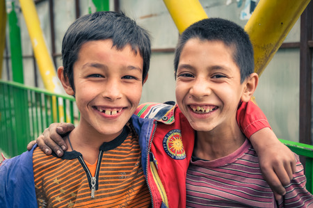 Kabul, Afghanistan - circa October 2011: Two young boys hold arms over their shoulders and smile joyfully to photocamera at marketplace in Old town, old city part in Kabul. Documentary editorial.のeditorial素材