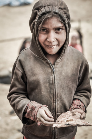 Dolpo, Nepal - circa June 2012: Young smiling girl in brown sweatshirt and hood poses during eating cake in Dolpo, Nepal. Documentary editorial.のeditorial素材