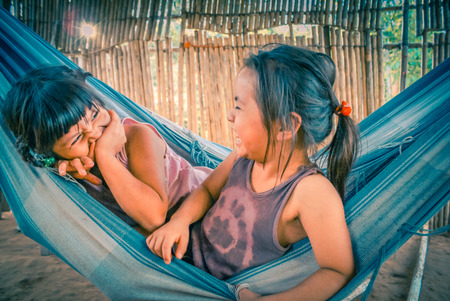 Villa Alcira, Bolivia -circa June 2009: Small smiling girls sit in hammock and laughs joyfully at Villa Alcira, Bolivia. Documentary editorial.のeditorial素材