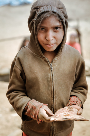 Dolpo, Nepal - circa June 2012: Young brown-eyed girl in brown sweatshirt and hood eats cake in Dolpo, Nepal. Documentary editorial.のeditorial素材