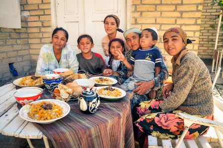 Bukhara, Uzbekistan - circa July 2011: Big native family sits at table and poses during lunch in Bukhara. Documentary editorial.のeditorial素材