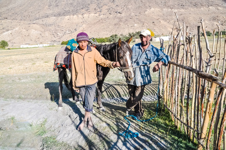 Khorog, Tajikistan - circa September 2011: Native father poses with his son in Khorog, Tajikistan. In photo with their brown horse. Documentary editorial.のeditorial素材