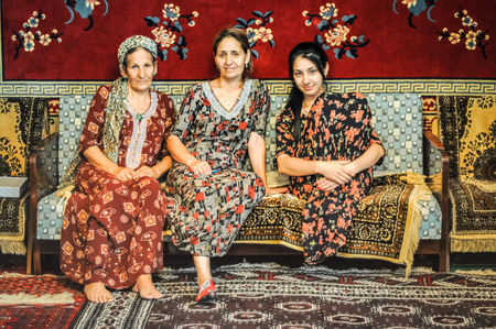 Ashgabat, Turkmenistan - circa July 2011: Women in beautiful dresses sit in room covered with amazing Turkmen carpets in Ashgabat, Turkmenistan. Documentary editorial.のeditorial素材