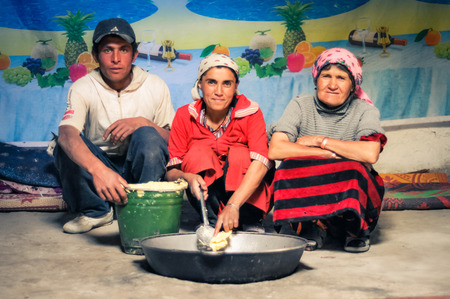 Wakhan valley, Tajikistan - circa October 2011: Native family kneels next to large pot in Wakhan valley, Tajikistan. Documentary editorial.のeditorial素材