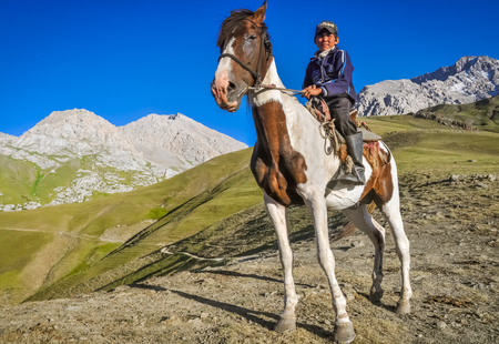 Arslanbob, Kyrgyzstan - circa July 2011: Native boy sits on brown and white spotted horse at top of hill in mountain range of Arslanbob, Kyrgyzstan. Documentary editorial.のeditorial素材