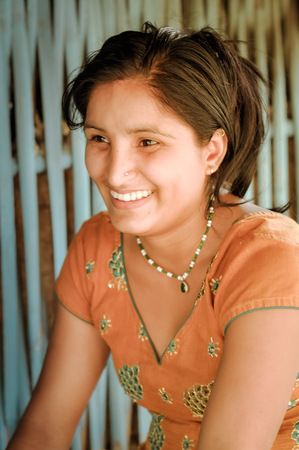 Damak, Nepal - circa May 2012: Young black-haired woman with piercing in her nose and with necklace wears orange dress and laughs at Nepali refugee camp in Damak, Nepal. Documentary editorial.のeditorial素材