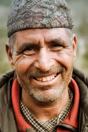 Dolpo, Nepal - circa June 2012: Brown-eyed man with cap dressed in red shirt and grey jacket with beard smiles nicely to photocamera in Dolpo, Nepal. Documentary editorial.のeditorial素材
