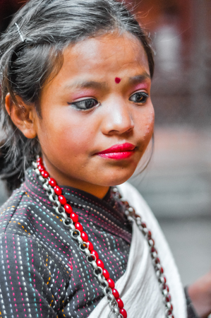 Kathmandu, Nepal - circa May 2012: Young girl with make-up on her face and red dot on forehead wears necklace and looks down in Kathmandu, Nepal. Documentary editorial.のeditorial素材