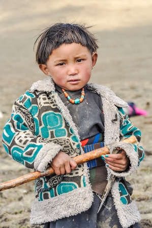 Dolpo, Nepal - circa June 2012: Small native girl with short black hair dressed in grey shirt and warm jacket wears colourful necklace made of beads in Dolpo, Nepal. Documentary editorial.のeditorial素材
