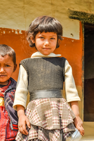 Beni, Nepal - circa May 2012: Pretty young girl with short brown hair wears brown dress and looks timidly to photocamera in streets of Beni, Nepal. Documentary editorial.のeditorial素材