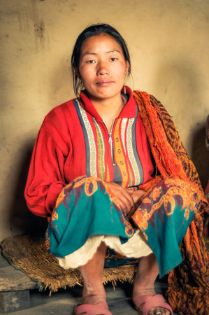 Kanchenjunga Trek, Nepal - circa May 2012: Woman in colourful clothes sits on small bench in Kanchenjunga Trek, Nepal. Documentary editorial.のeditorial素材