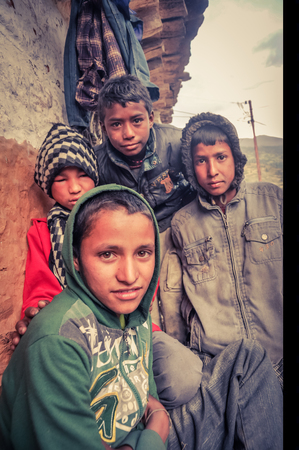 Dolpo, Nepal - circa June 2012: Four young boys with caps or hood sit near wall of house and look curiously to photocamera in Dolpo, Nepal. Documentary editorial.のeditorial素材