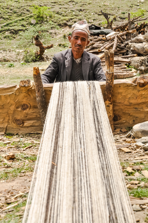 Dolpo, Nepal - circa June 2012: Photo of native man in black jacket and brown cap sitting outside and weaving in Dolpo, Nepal. Documentary editorial.のeditorial素材