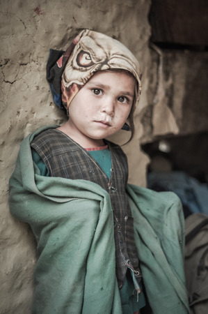 Beni, Nepal - circa May 2012: Young native girl with headcloth leans on wall in their house and covers herself in green blanket in Beni, Nepal. Documentary editorial.のeditorial素材