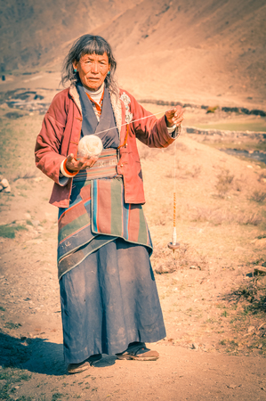 Dolpo, Nepal - circa June 2012: Old grey-haired woman wears red jacket and grey kimono with ball of wool in hand in Dolpo, Nepal. Documentary editorial.のeditorial素材