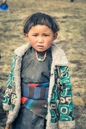 Dolpo, Nepal - circa June 2012: Small native girl with short black hair dressed in grey kimono with large belt and warm jacket wears necklace made of beads in Dolpo, Nepal. Documentary editorial.のeditorial素材