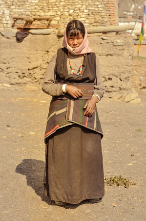Dolpo, Nepal - circa June 2012: Timid black-haired woman in brown dress with pink headcloth wears colourful necklace made of beads and poses outside in Dolpo, Nepal. Documentary editorial.のeditorial素材