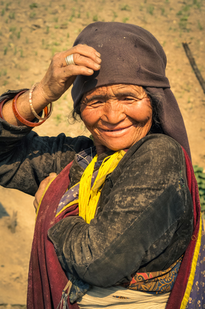 Dolpo, Nepal - circa May 2012: Old native woman with wrinkled face and brown headcloth holds her hand on head in Dolpo, Nepal. Documentary editorial.のeditorial素材