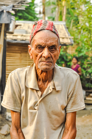 Damak, Nepal - circa May 2012: Old man with wrinkles dressed in brown shirt with cap on his head frowns to photocamera at Nepali refugee camp in Damak, Nepal. Documentary editorial.のeditorial素材