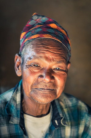 Beni, Nepal - circa May 2012: Photo of native man in shirt with wrinkled face and colourful cap on his head smiling modestly to photocamera in Beni, Nepal. Documentary editorial.のeditorial素材
